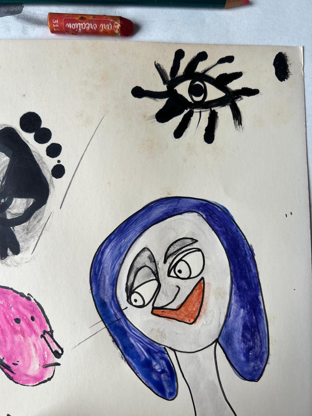 Working sheet: a face inside a heavy blue brushed hood with an orange-red mouth, a large black painted eye above it, a pink form at the left edge, with a pencil and an orange crayon lying on the paper