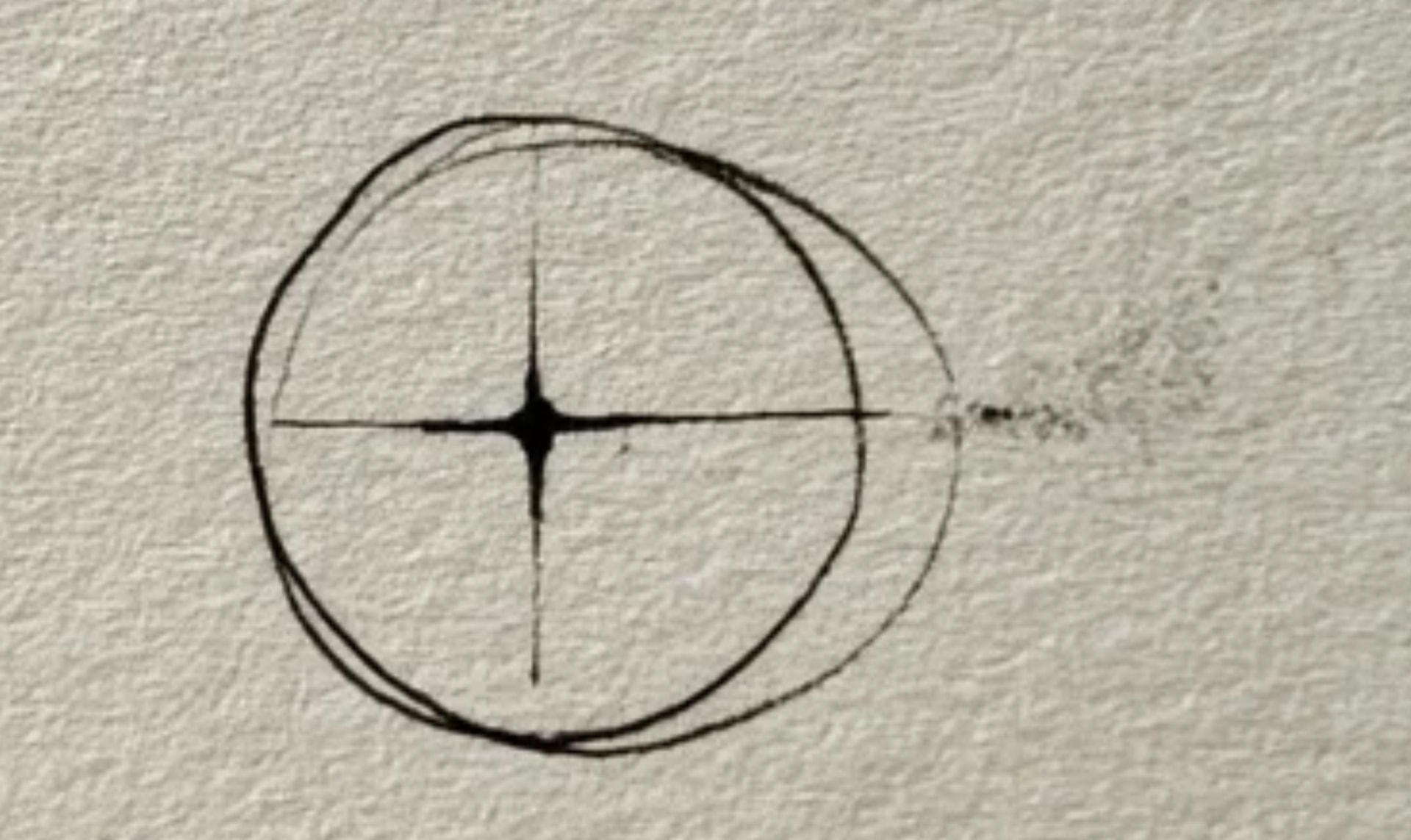 Hand-drawn ink registration mark: a circle with crosshairs on textured paper