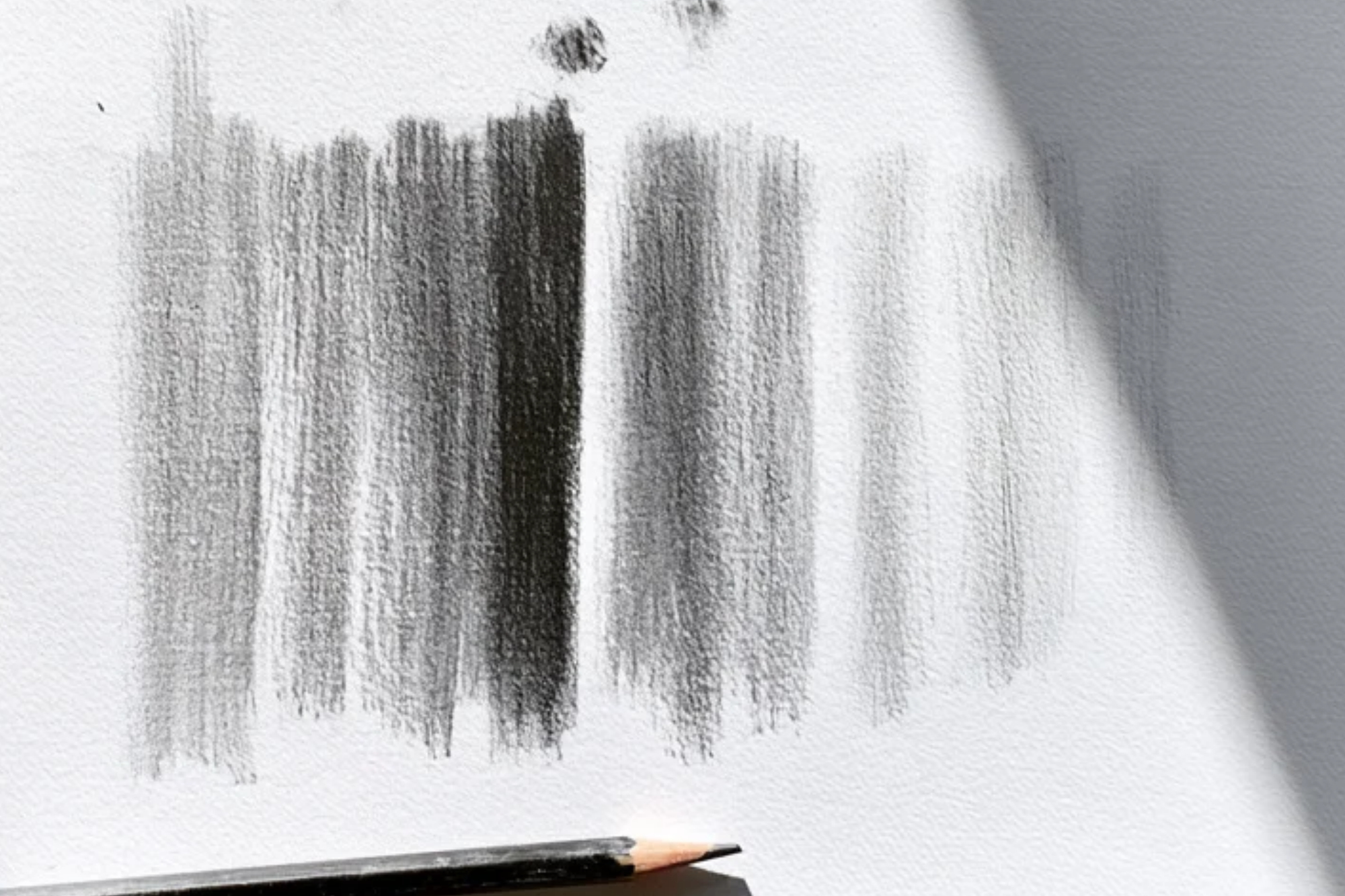 Bands of graphite shading at different pressures on textured paper, with a sharpened pencil resting below.