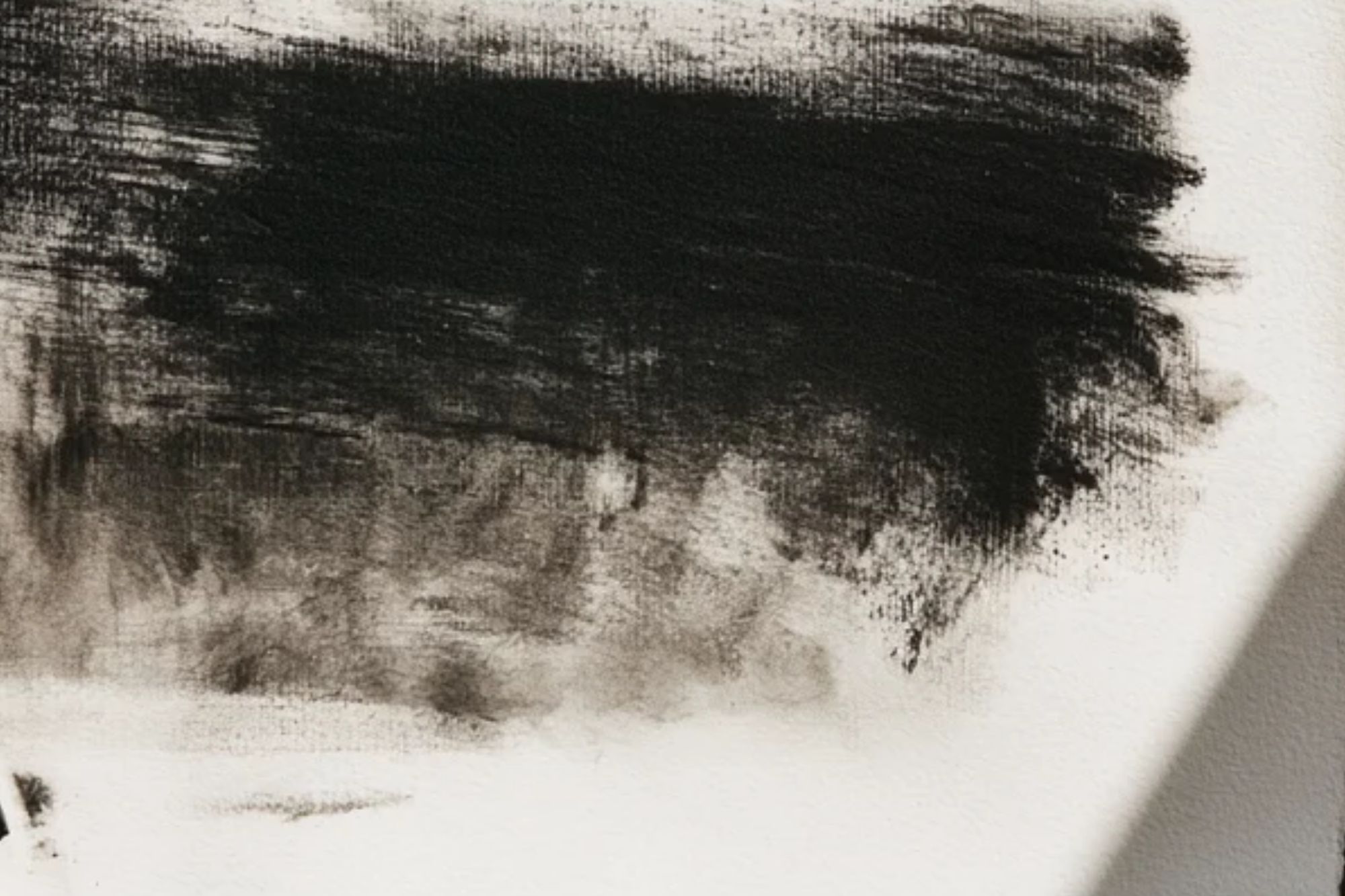 A dense black charcoal mass on paper fading into smudged grey and soft edges.